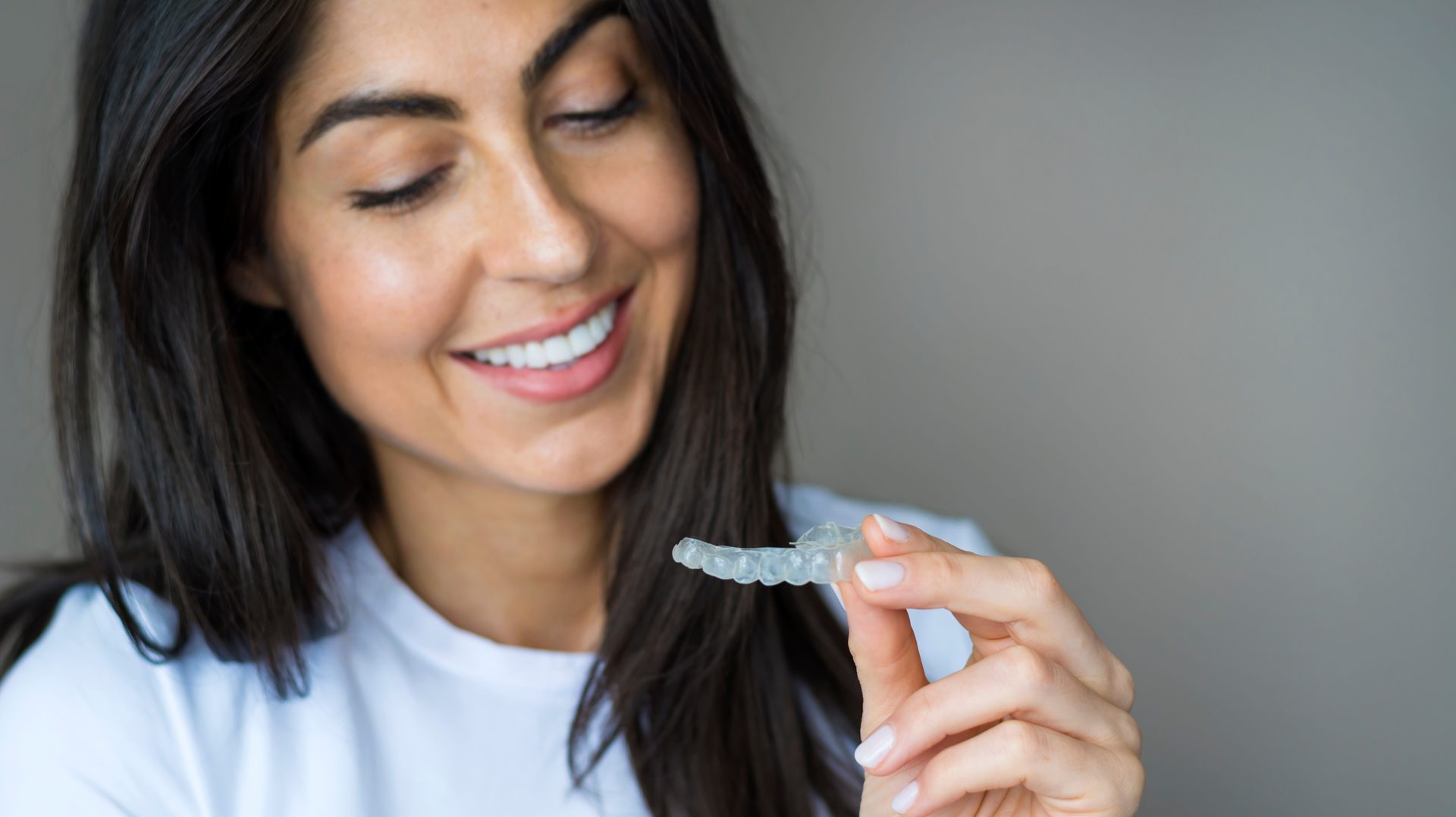 A smiling woman holding a clear aligner